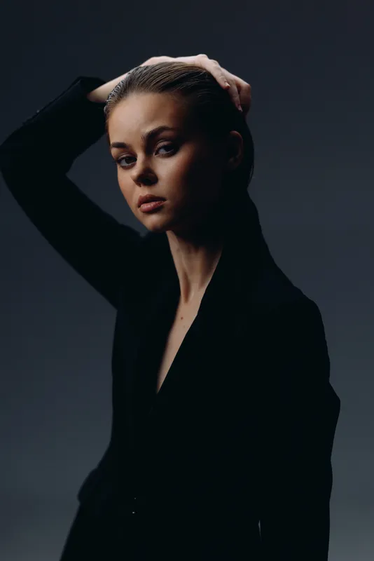 Portrait of thoughtful woman with hand in hair wearing black clothing in dark studio lighting.