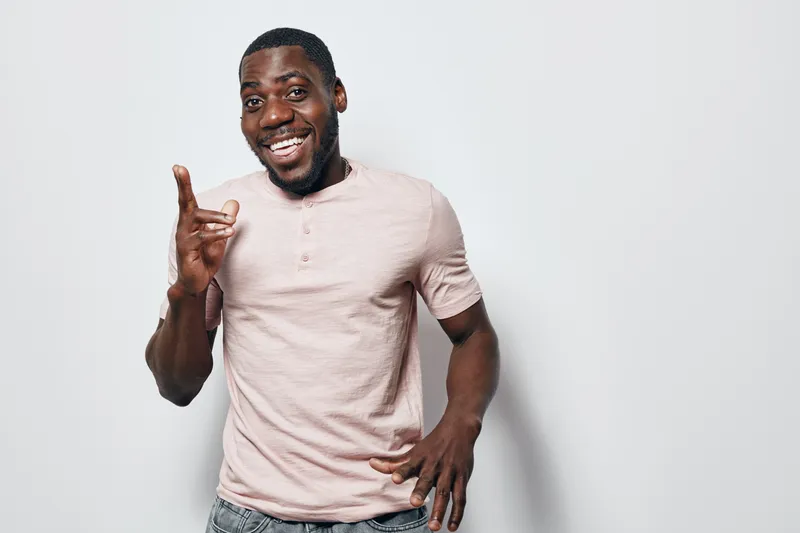 African American man with dark skin smiling and pointing finger up wearing casual light pink shirt standing against white background. Happy male portrait with positive gesture and confident