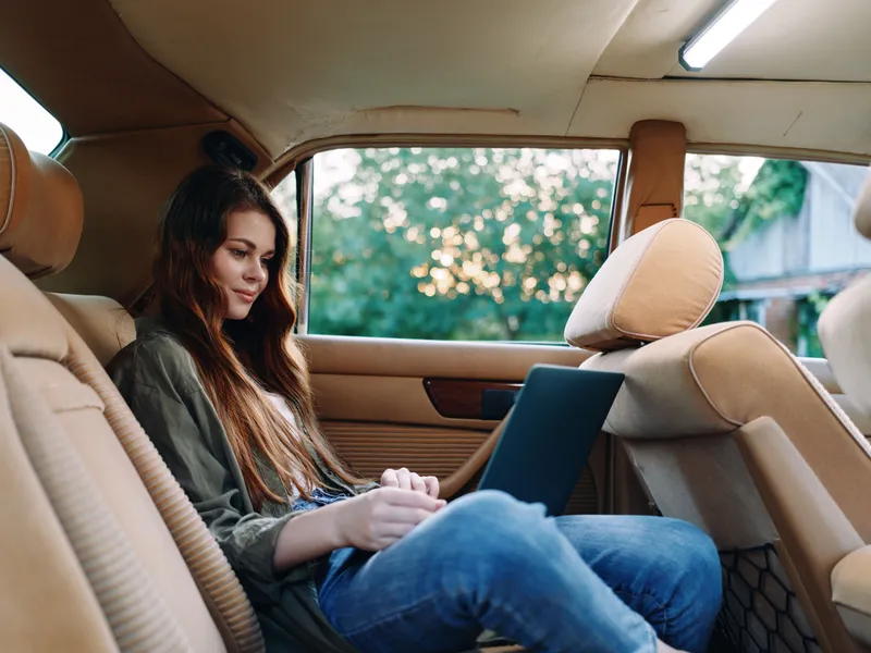 Young woman working on a laptop in a vintage car interior, showcasing a relaxed and productive vibe with natural lighting and earthy tones.