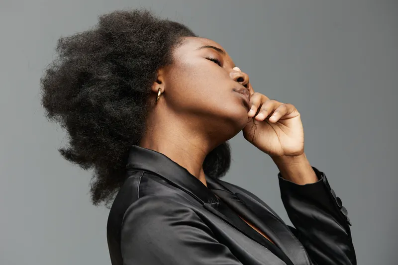 Confident African woman in stylish black suit, showcasing natural beauty and poise against a minimalist gray background, ideal for empowerment themes