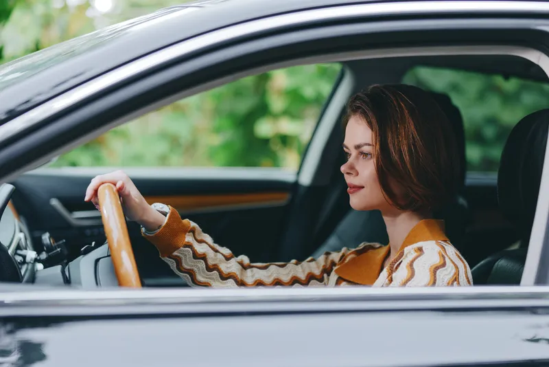 Portrait of a woman driving a car, gripping the steering wheel with calm focus, seated in a stylish interior.