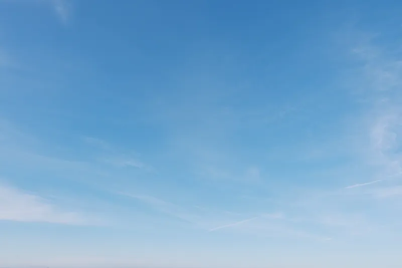 Blue sky with wispy clouds stretches over a calm horizon, presenting an expansive outdoor scene filled with serenity, light and natural air, ideal for nature, travel and minimalistic branding.