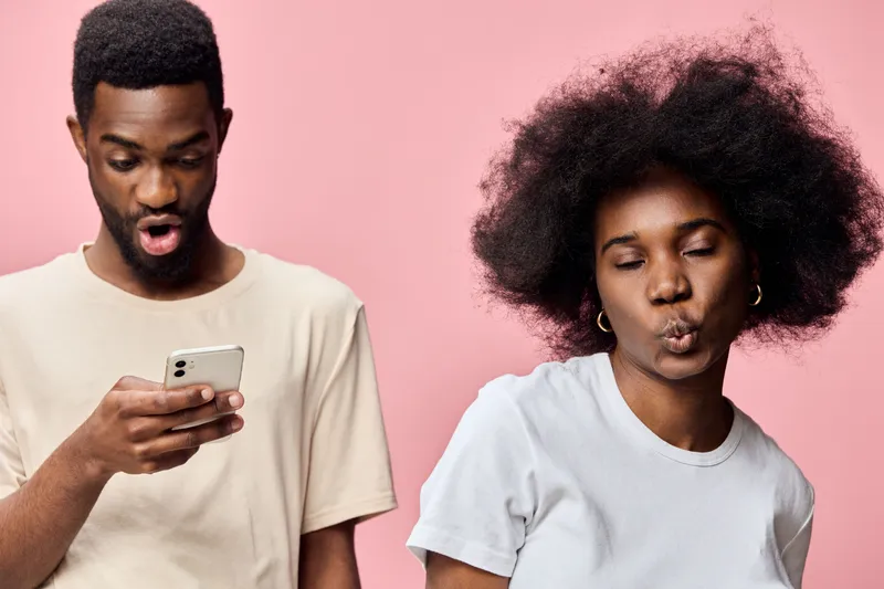 Stylish Afro American couple with playful expressions against a pastel pink background, showcasing modern fashion and vibrant emotions in a youthful, trendy context