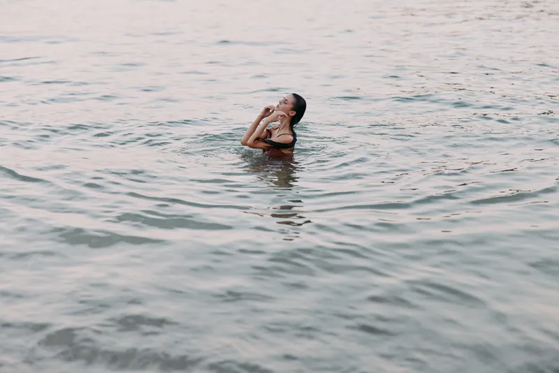 Woman swimming in calm water with peaceful expression, enjoying outdoor activity and summer tranquility by the shore.