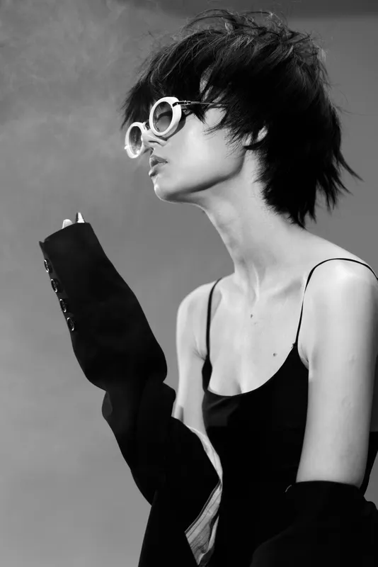 Black and white portrait of a stylish woman in sunglasses with short hair and elegant attire, capturing modern fashion and mood.
