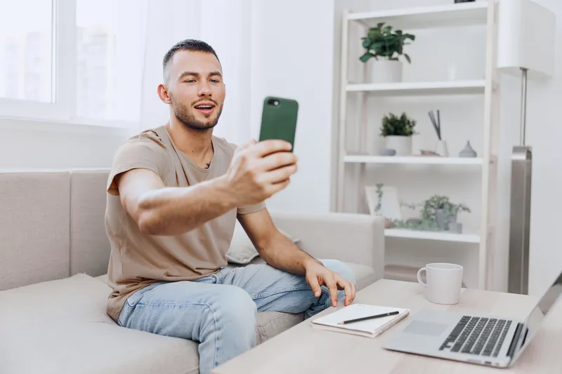 Smiling man engaged in a phone call, embracing emotional connection while practicing digital detox at home, surrounded by a minimalist workspace and soft colors.