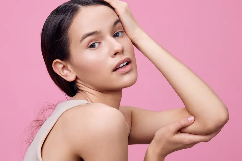 Natural beauty portrait of a young woman with a soft expression against a pink background, showcasing minimalist style and grace, perfect for advertising beauty products
