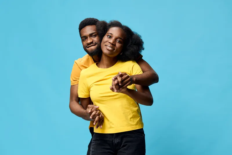 Happy couple in matching yellow shirts against a blue background, showcasing love and connection through joyful expressions and playful poses