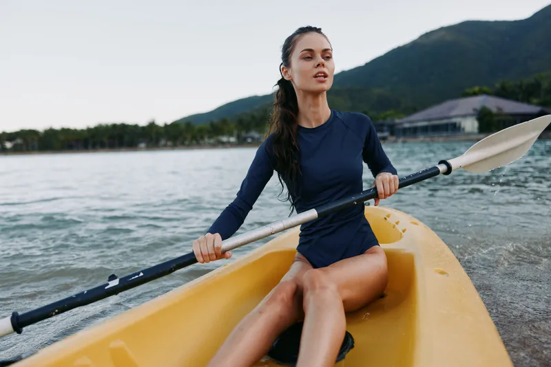 Focused paddler sits in a yellow kayak, gliding across calm lake waters as distant mountains rise, capturing motion, balance, and outdoor adventure.