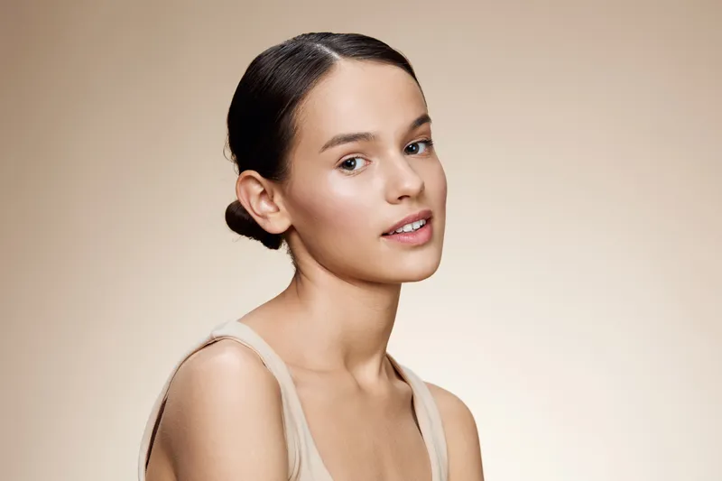 Young woman with natural makeup showcasing healthy skin, soft expression, and neutral background for beauty and skincare concepts