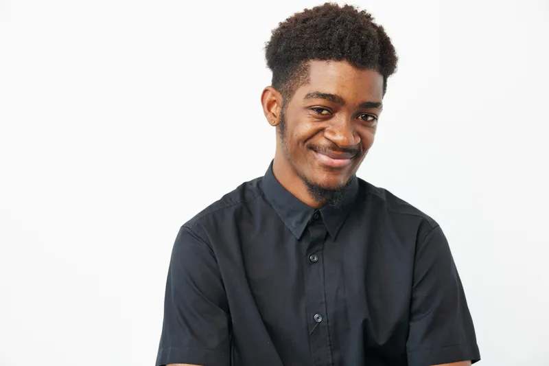 Smiling African American man dressed in a stylish black shirt, showing warmth and friendliness against a minimalist white background.