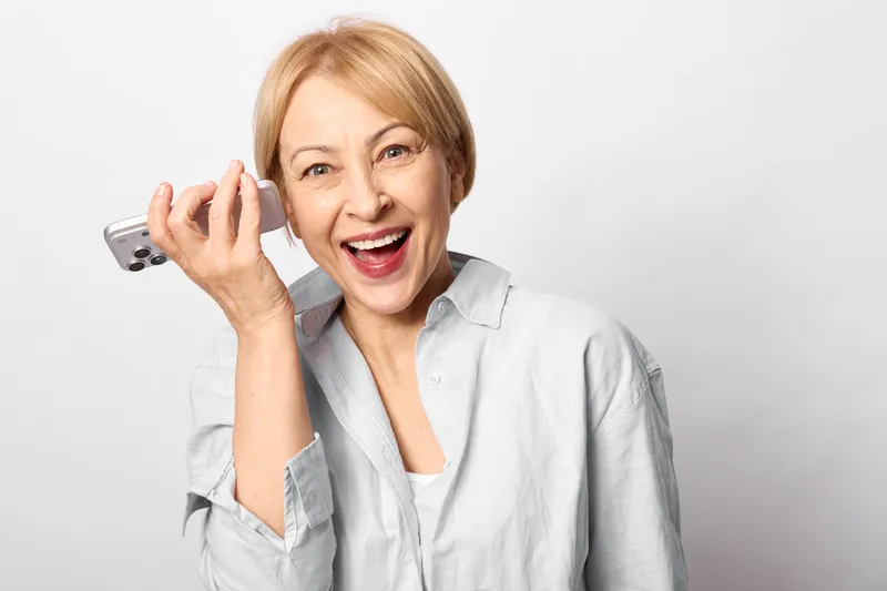 Smiling senior woman holding smartphone and medication blister, white background, close up portrait, telemedicine concept, health care and wellness, soft light, calm mood