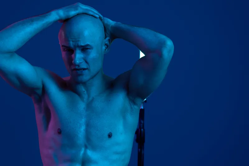 Handsome man with a muscular build, posing under dramatic blue light, showcasing strength and emotion in a striking, captivating composition.