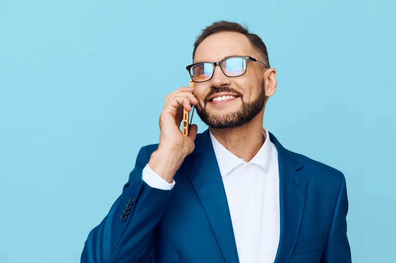 A professional business man against a vivid colored background, smiling while on a mobile call, projecting confidence, optimism, and focused communication.