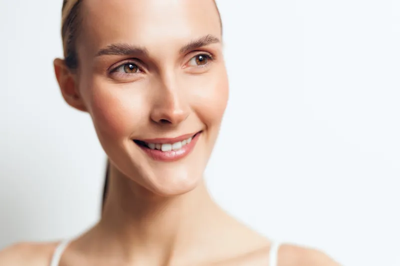 A close up portrait of one person, a young adult woman with a brunette, hair pulled back, wearing a white tank top against a bright white background, conveying a approachable, confident wellness vibe.