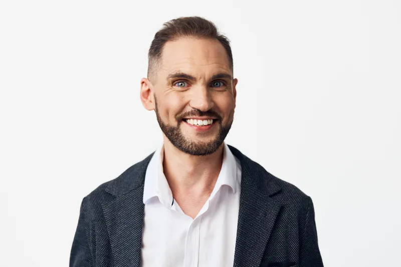 A confident business professional man smiles warmly on a isolated white background, projecting approachability, focus, and motivation in a clean corporate setting.