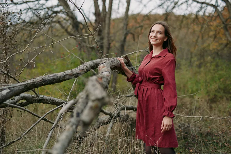Candid portrait of a smiling woman in a red dress leaning on a fallen tree in a wild meadow, natural light and relaxed pose conveying authenticity and a genuine emotional presence.