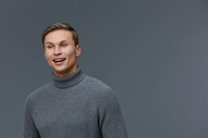 Smiling man young adult caucasian male in gray knit sweater looking to side shot isolated on plain gray background studio portrait. People lifestyle concept