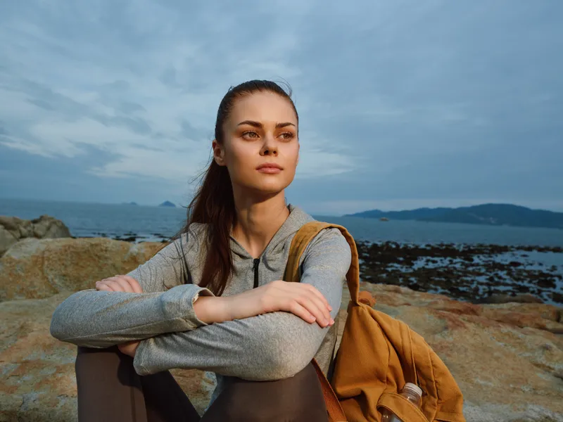 Woman in a gray hoodie relaxing by the seaside, showcasing serenity and connection with nature, perfect for travel and lifestyle themes