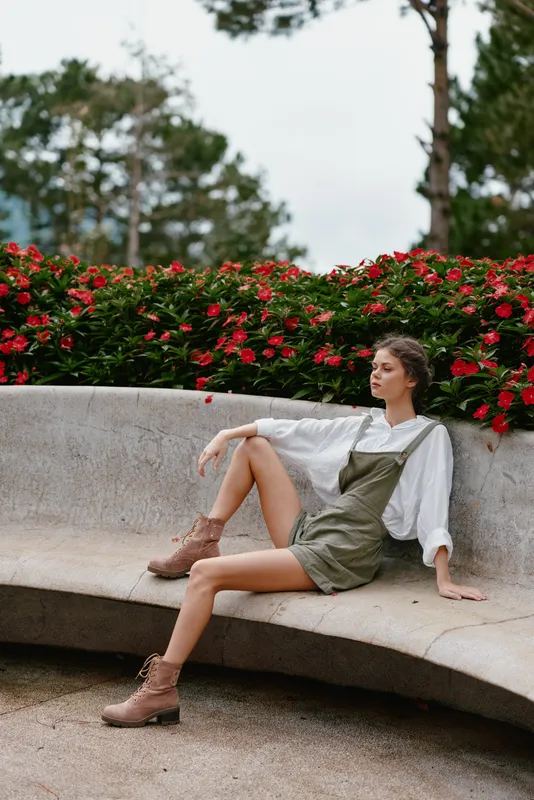 Stylish young woman in casual outfit sitting on a curved bench surrounded by blooming flowers, showcasing confidence and elegance