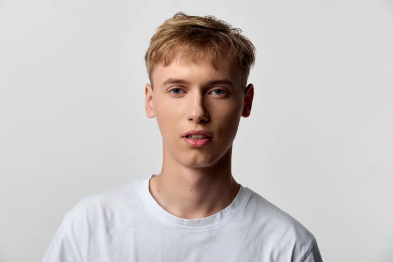 Young man wearing a white tee against a neutral backdrop, close up facial expression, casual studio shot for fashion, clean minimal background suitable for lifestyle branding