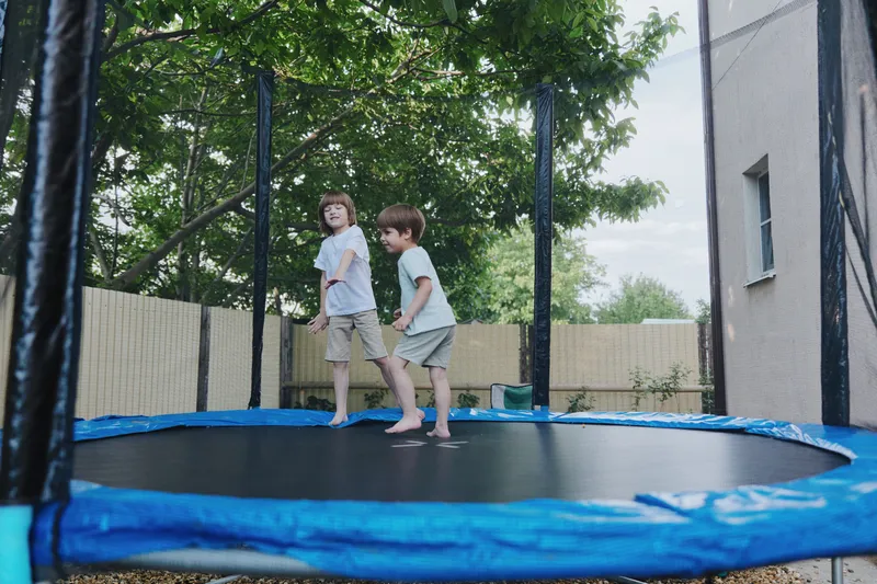 Playful children bouncing on a trampoline, showcasing joy and excitement in a vibrant outdoor setting under lush greenery. ###