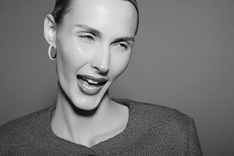 Close-up portrait of a young white woman with fair skin winking and smiling confidently. Studio shot with smooth lighting, concept of beauty, fashion, and playful expression.