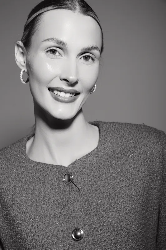 Smiling caucasian woman with fair skin and slicked back hair wears textured jacket and hoop earrings in studio portrait. Concept of beauty and elegance.