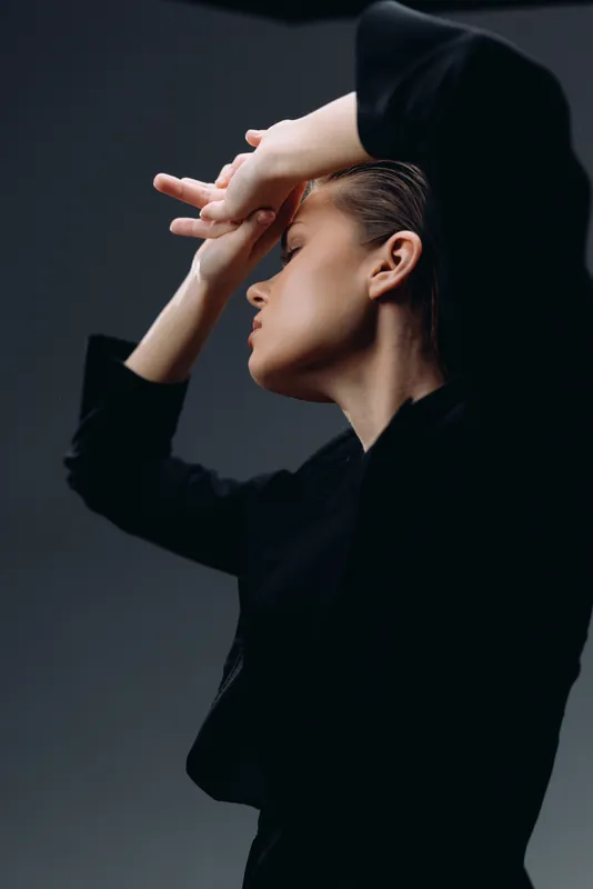 Profile of a woman in black clothing with hands raised showing expression and elegance in studio light