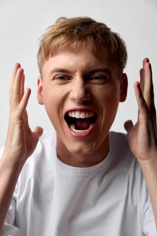 Excited man shouting, hands up, open mouth in studio setting showcasing bold energy and intense emotion for dynamic expressive moments suitable for advertising and campaigns