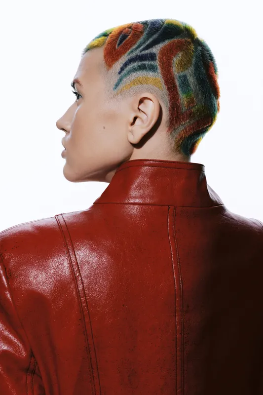 Woman with colorful geometric shaved hairstyle in red leather jacket, side profile view, artistic fashion portrait with bold style and creative urban vibe.