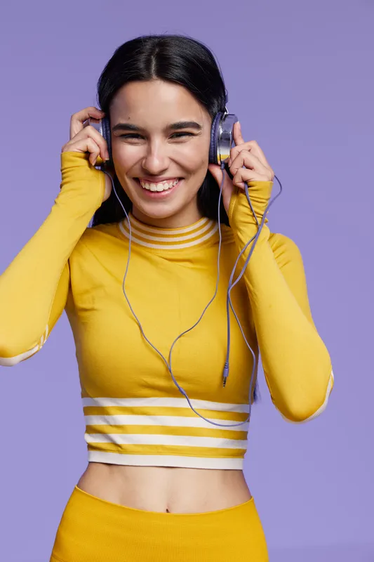 sport fitness woman smiling and enjoying music wearing yellow activewear with headphones against purple background, healthy lifestyle, workout motivation