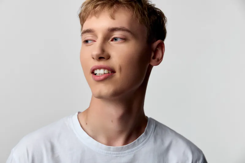 Young man, casual style, white t shirt against neutral backdrop, warm lighting and relaxed smile conveying confidence, freshness and approachable vibe for lifestyle and fashion projects