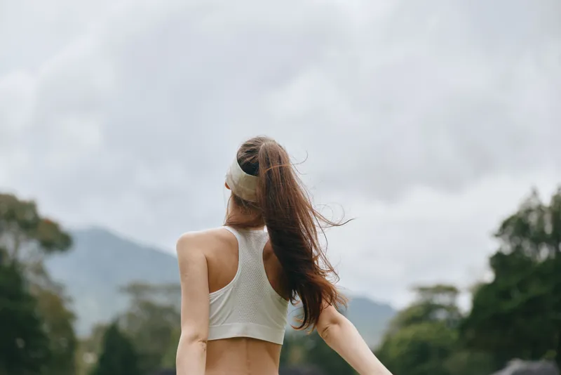 Joyful young woman in a sporty outfit enjoying outdoor exercise during a cloudy day, showcasing health and vitality in a natural setting