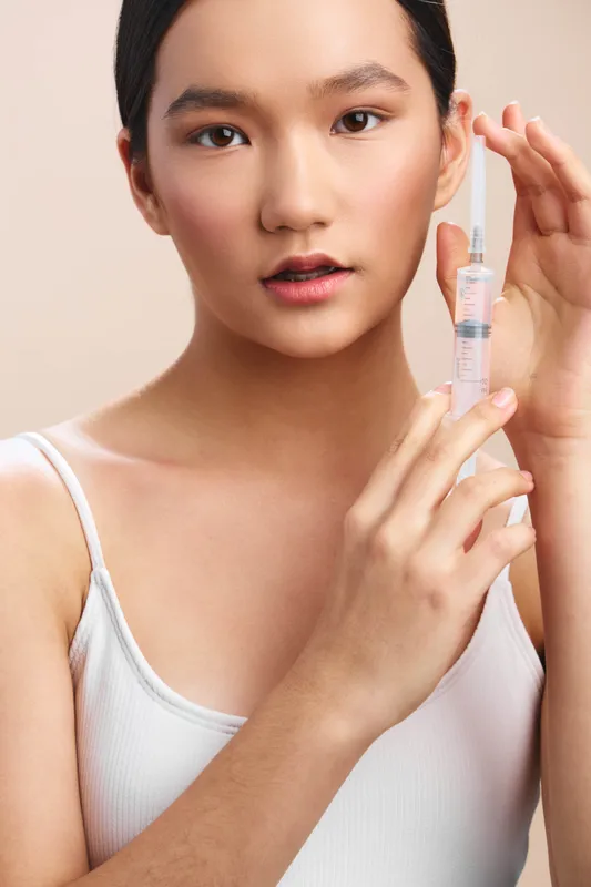 Asian woman prepares a syringe with calm focus in a clean clinical setting, showcasing healthcare professionalism and a careful, precise approach to treatment.