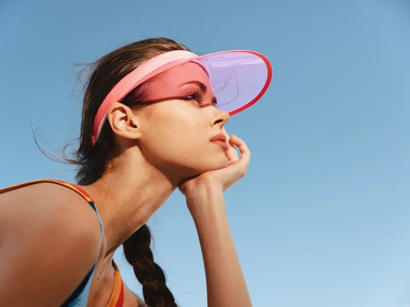 Female athlete wearing a pink visor gazes toward the distance on a clear sunny day, capturing focus, form, and a bright, energetic moment that evokes energy and movement.