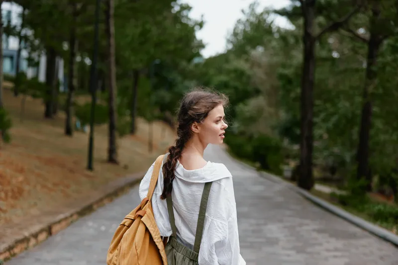 Young woman walking in a nature filled park, wearing casual outfit and backpack, expressing calmness and contemplation in a serene setting