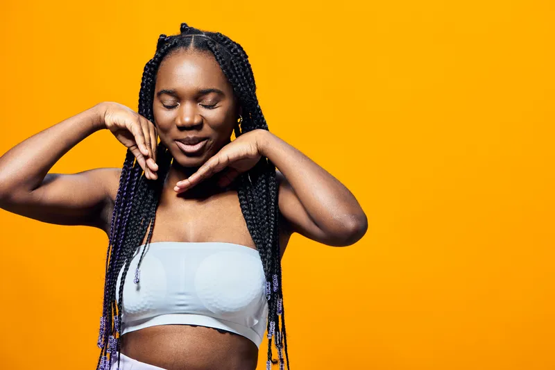 Joyful young woman with braided hair smiling against a vibrant orange background, showcasing a carefree and positive attitude in casual summer clothing