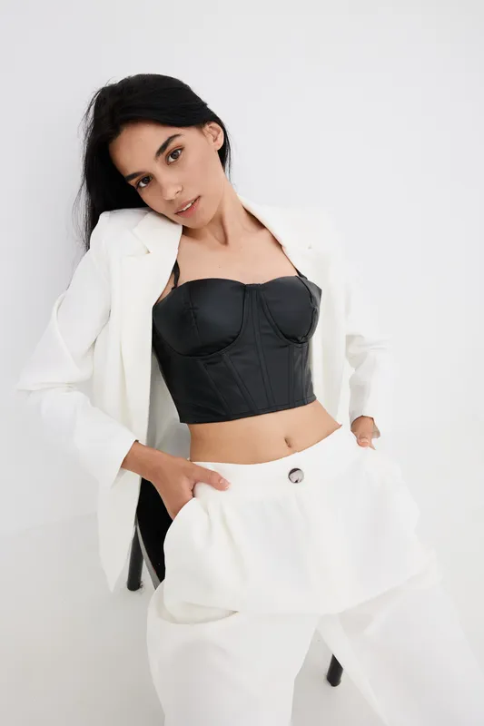 young woman posing in stylish black corset and white suit, modern fashion, confident posture, minimalistic light background, trendy outfit combination