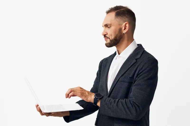 A professional man stands against a vibrant color background, focused and confident while using a laptop. Emotions of determination and poise convey business expertise and leadership in action.