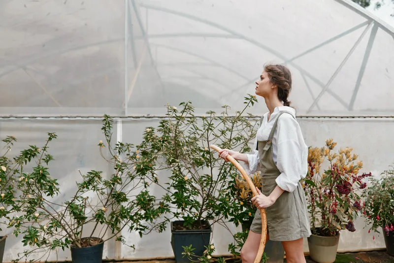 Young woman gardening in a greenhouse, wearing a casual outfit, showcasing the joy of nurturing plants in a vibrant, green environment