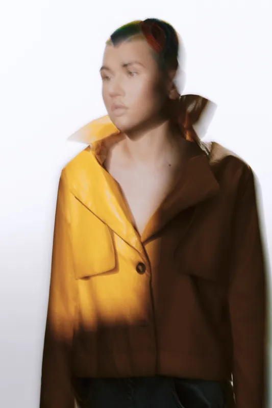 Artistic portrait of a woman in a yellow jacket with soft blur effect, creating a mysterious and creative mood against a light background.
