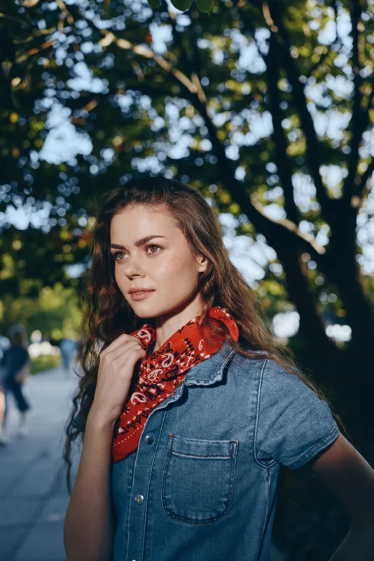 Lifestyle woman wearing modern boho-western denim street style with a red bandana, captured in warm natural light and film color effect, showcasing casual outdoor fashion.