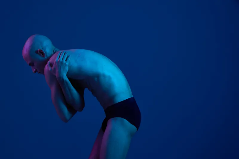 Male figure in blue light, showcasing an artistic pose. The image focuses on body expression and emotion, highlighting vulnerability and strength in a captivating way. ###