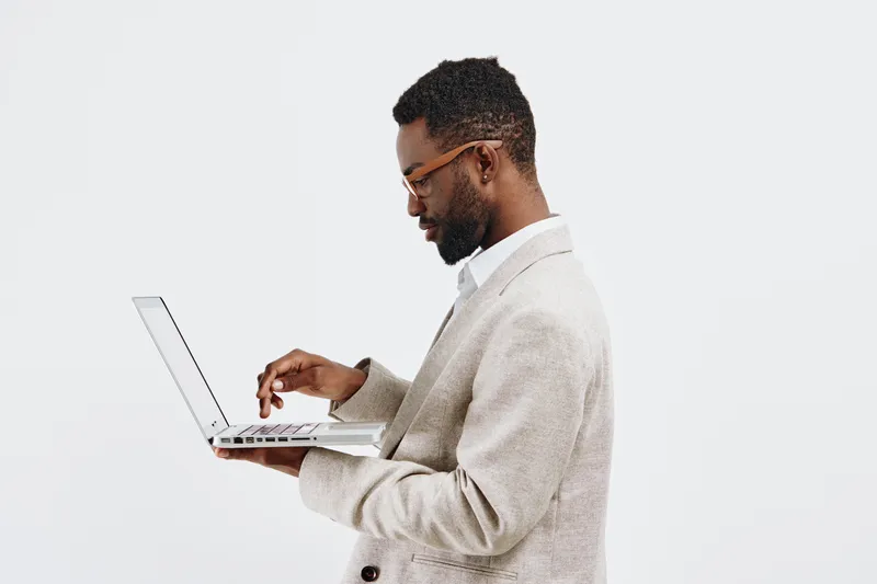 Man using laptop computer on plain white background, side view, professional workspace, casual attire, focused expression, modern technology, vertical shot, clean aesthetic. People lifestyle concept