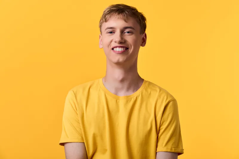 Yellow shirt, smiling male in studio against a bright background, showcasing casual fashion for lifestyle, marketing and product promotion in stock photography