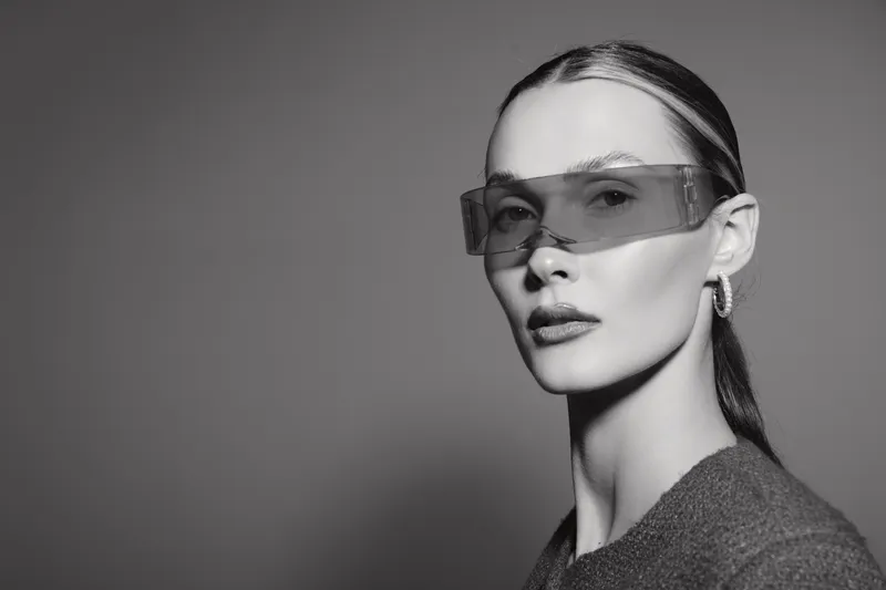 Young caucasian woman with pale skin wearing transparent glasses and hoop earrings looks confidently in studio. Concept of fashion, style, and modern accessories.