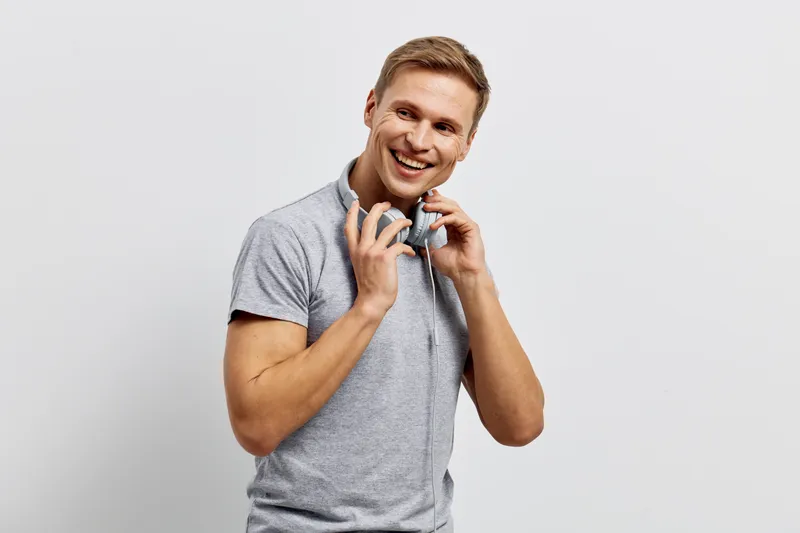 smiling young caucasian man in grey polo shirt holding headphones isolated on light background digital nomad concept technology communication