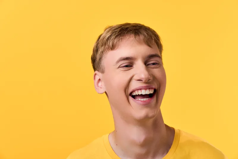 Smiling man with bright yellow background, casual attire, conveying happiness and friendly energy for lifestyle, social media, or marketing campaigns, ideal for upbeat advertising and approachable
