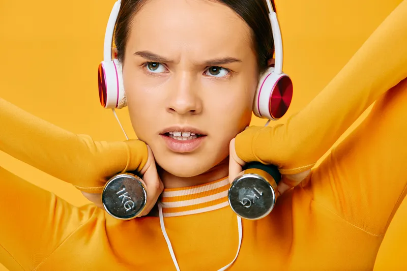 Fitness woman in bright orange athleticwear lifts dumbbells in a bold studio setting, showcasing strength, focus and motivation during an energetic workout.